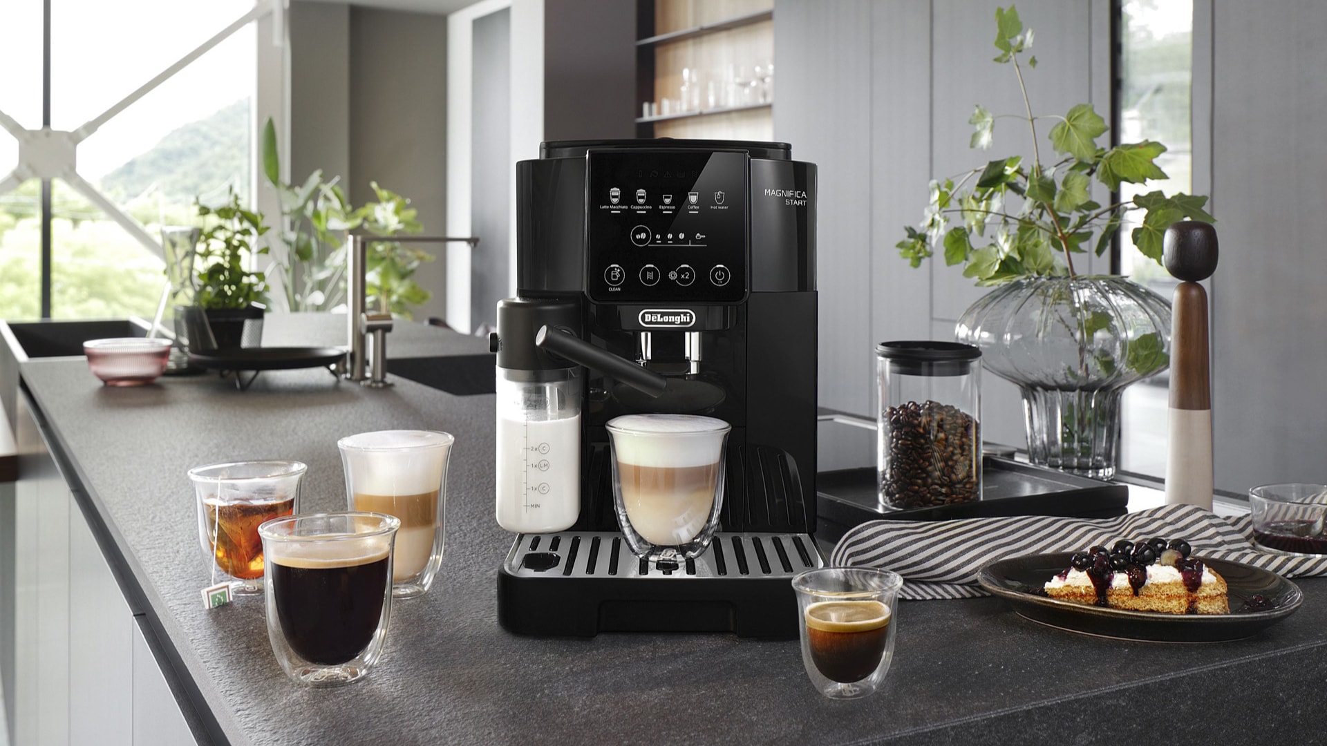 Machine espresso Magnifica Start de De’Longhi sur un comptoir de cuisine contemporaine, entourée de différentes boissons café préparées à la maison.