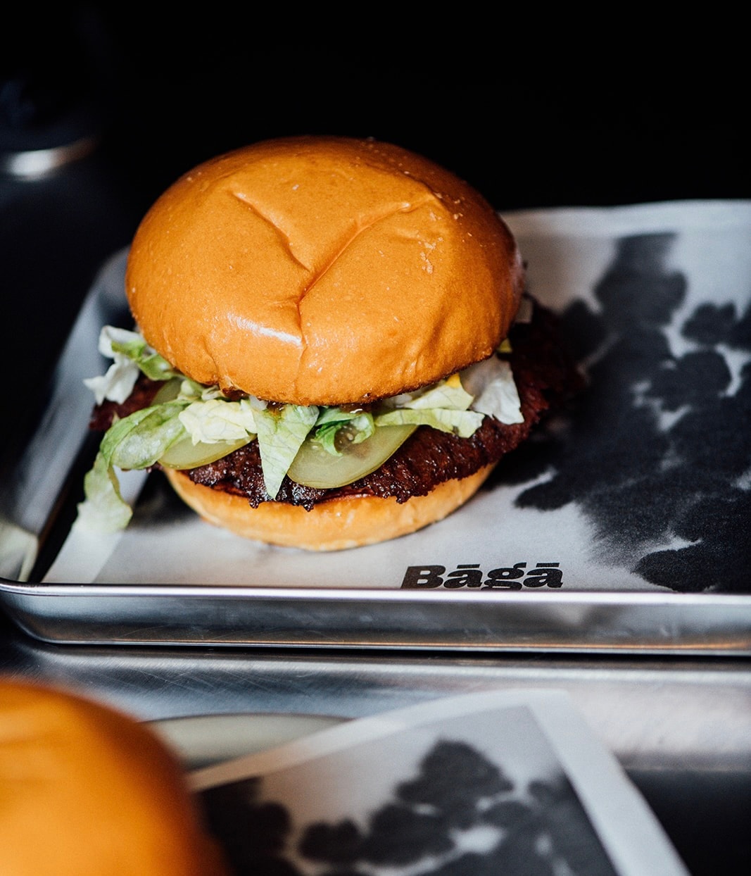 Smash burger au bœuf servi chez Bāgā à Montréal avec laitue, cornichons et pain brioché dans une approche inspirée de la culture japonaise