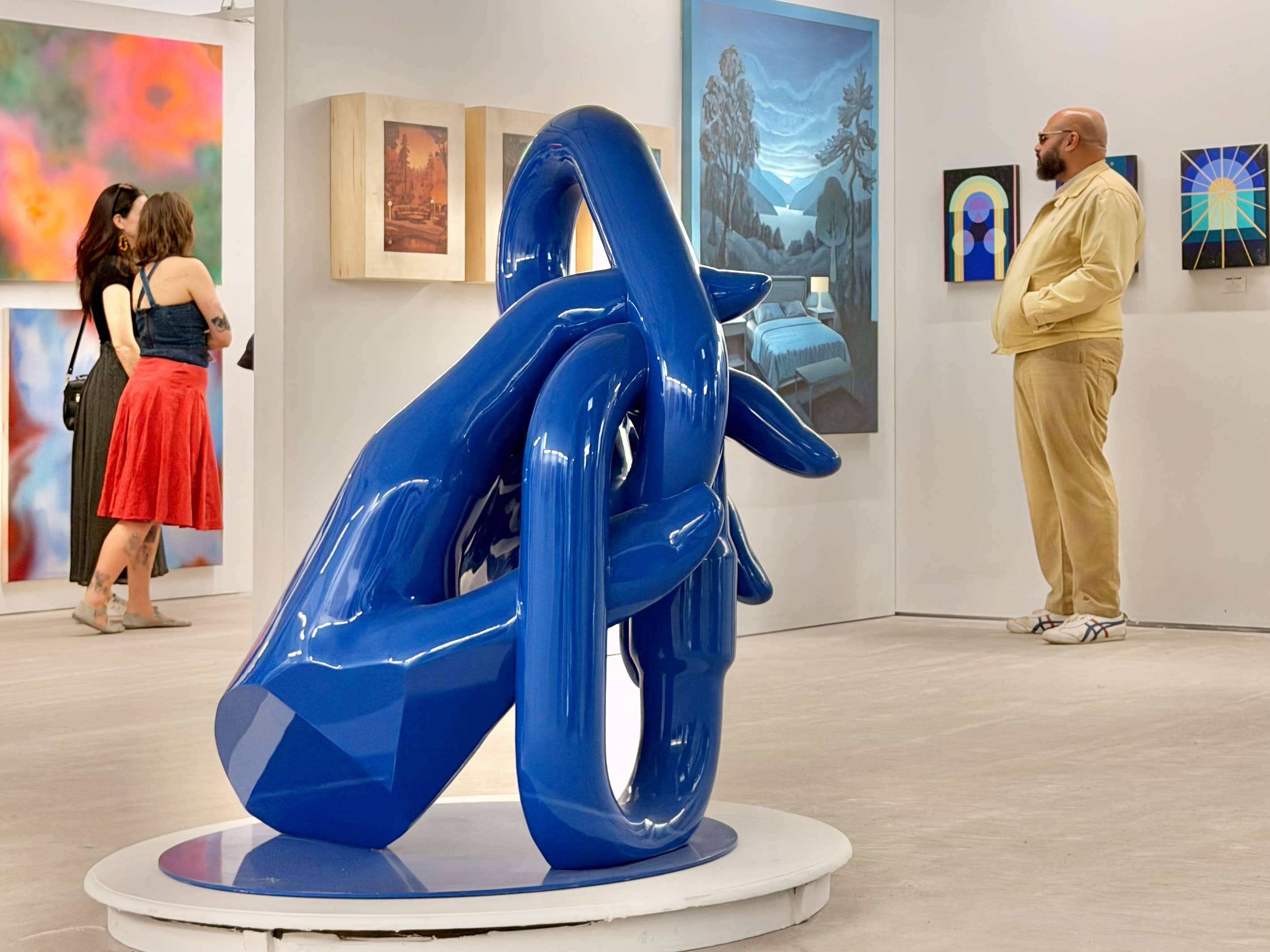 Grande sculpture bleue aux formes entrelacées présentée à Foire Parallèle 2026 devant des œuvres d’art contemporain et des visiteurs.