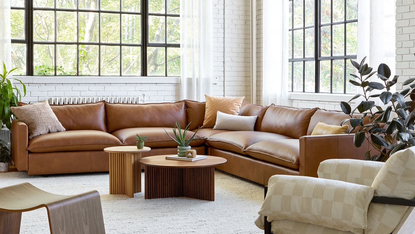 Canapé en cuir brun de Gus* Modern présenté dans un salon lumineux aux grandes fenêtres.