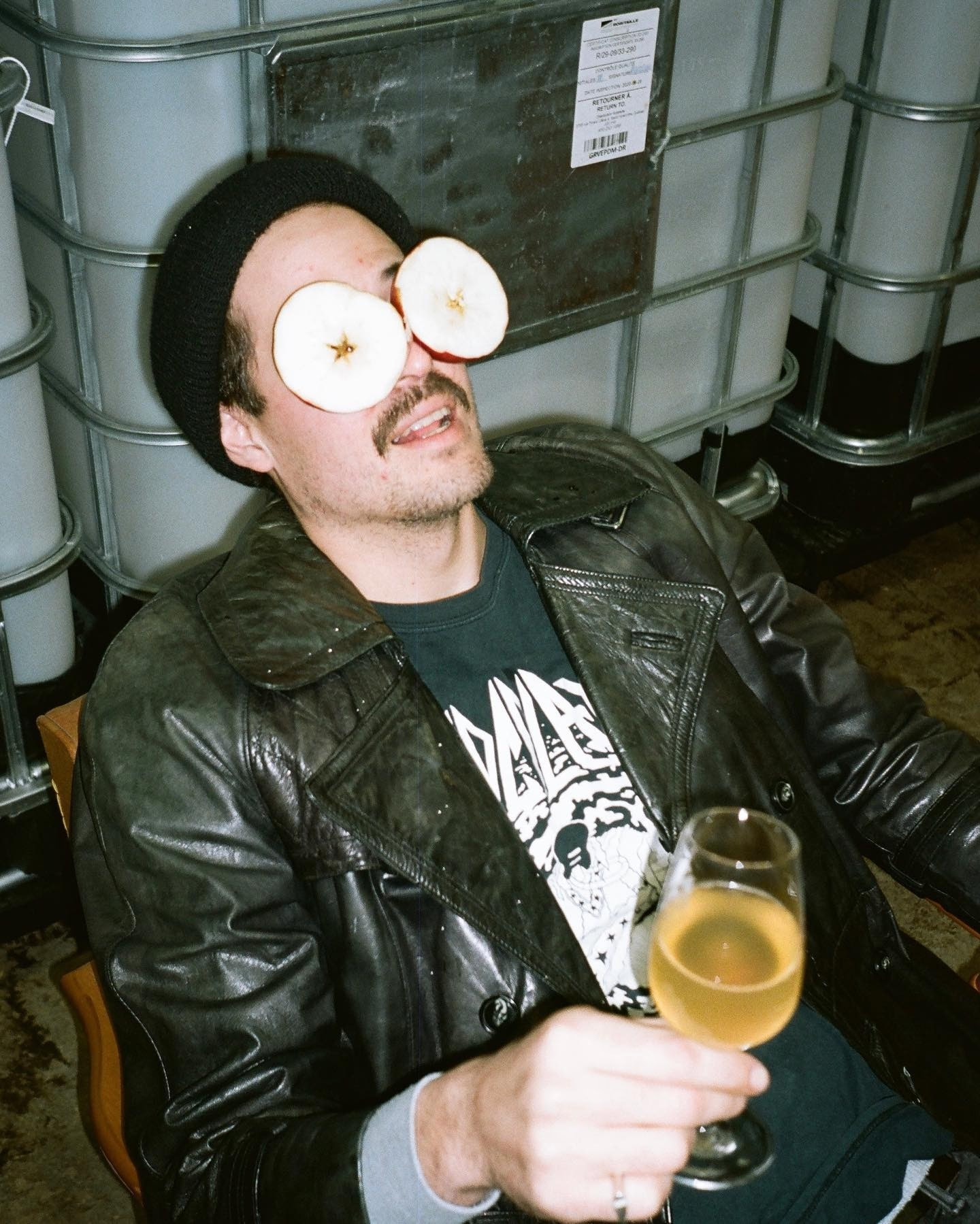 Producteur de Cidre Intrus tenant un verre de cidre avec deux demi-pommes devant les yeux dans l’espace de production de la cidrerie.