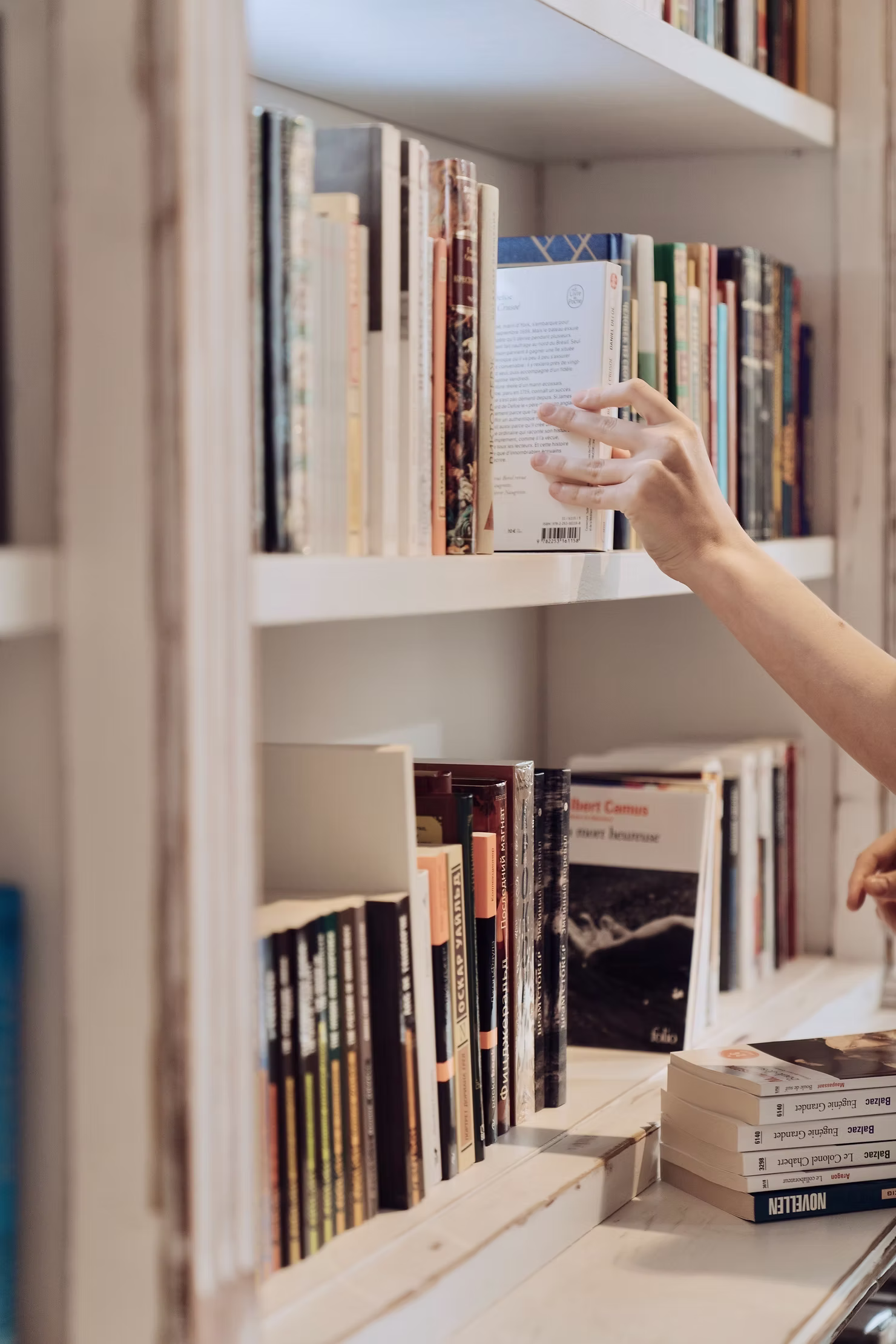 Main retirant un livre d’une bibliothèque dans un intérieur épuré et organisé.