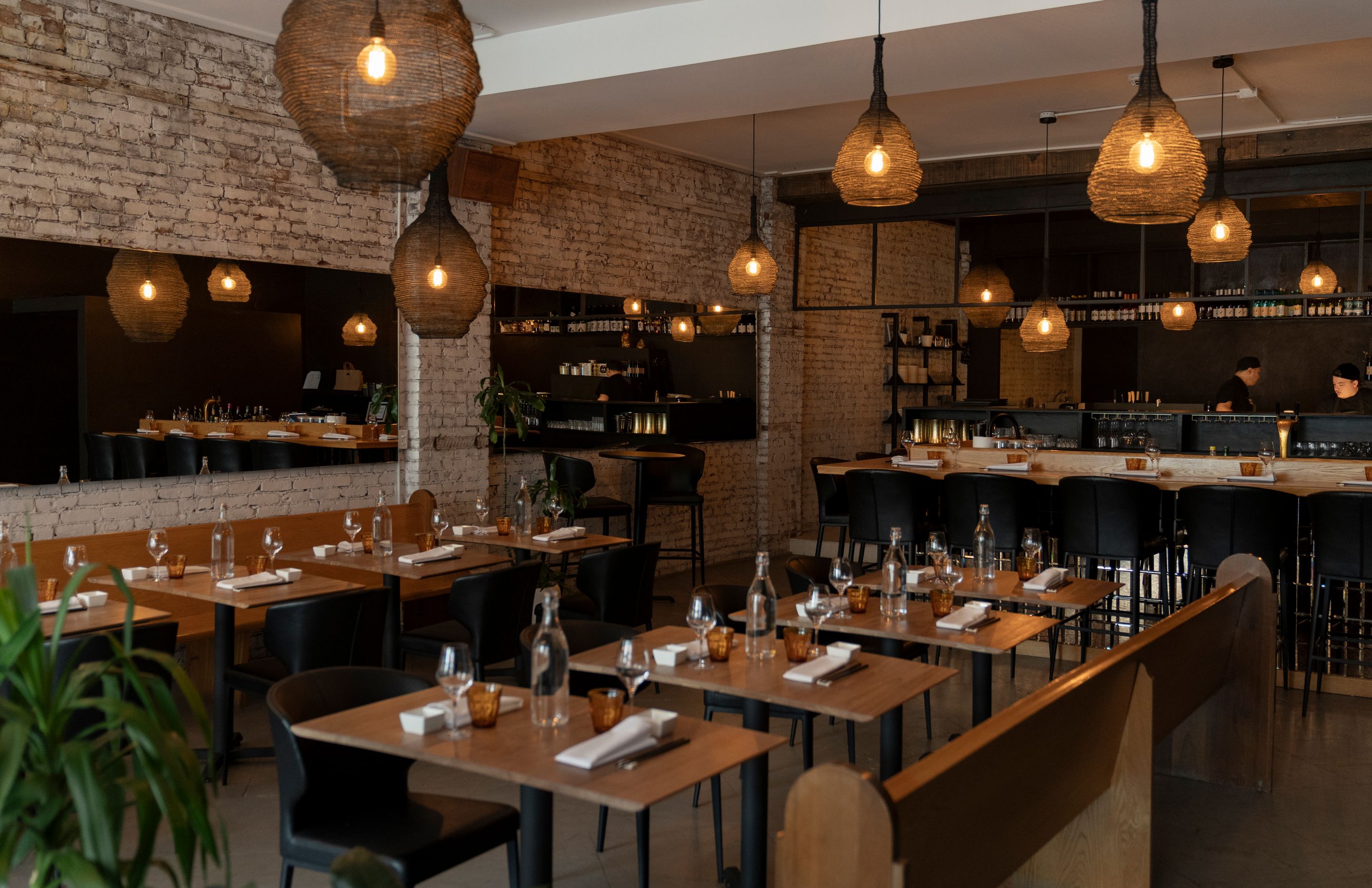Salle à manger du restaurant Tamisé à Montréal avec murs de briques, tables en bois et suspensions tressées.