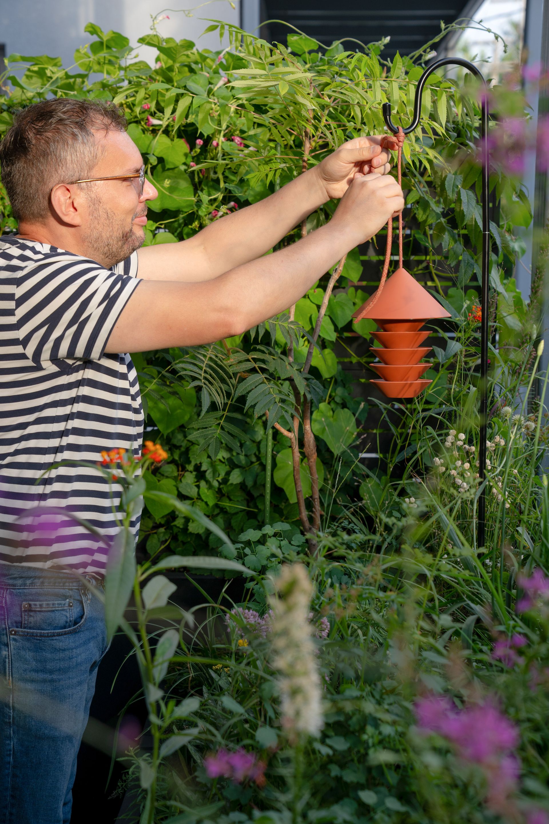 La mangeoire à oiseaux Silo Bird Feeder de Pidät, distribuée par Goodee, suspendue dans un jardin luxuriant.