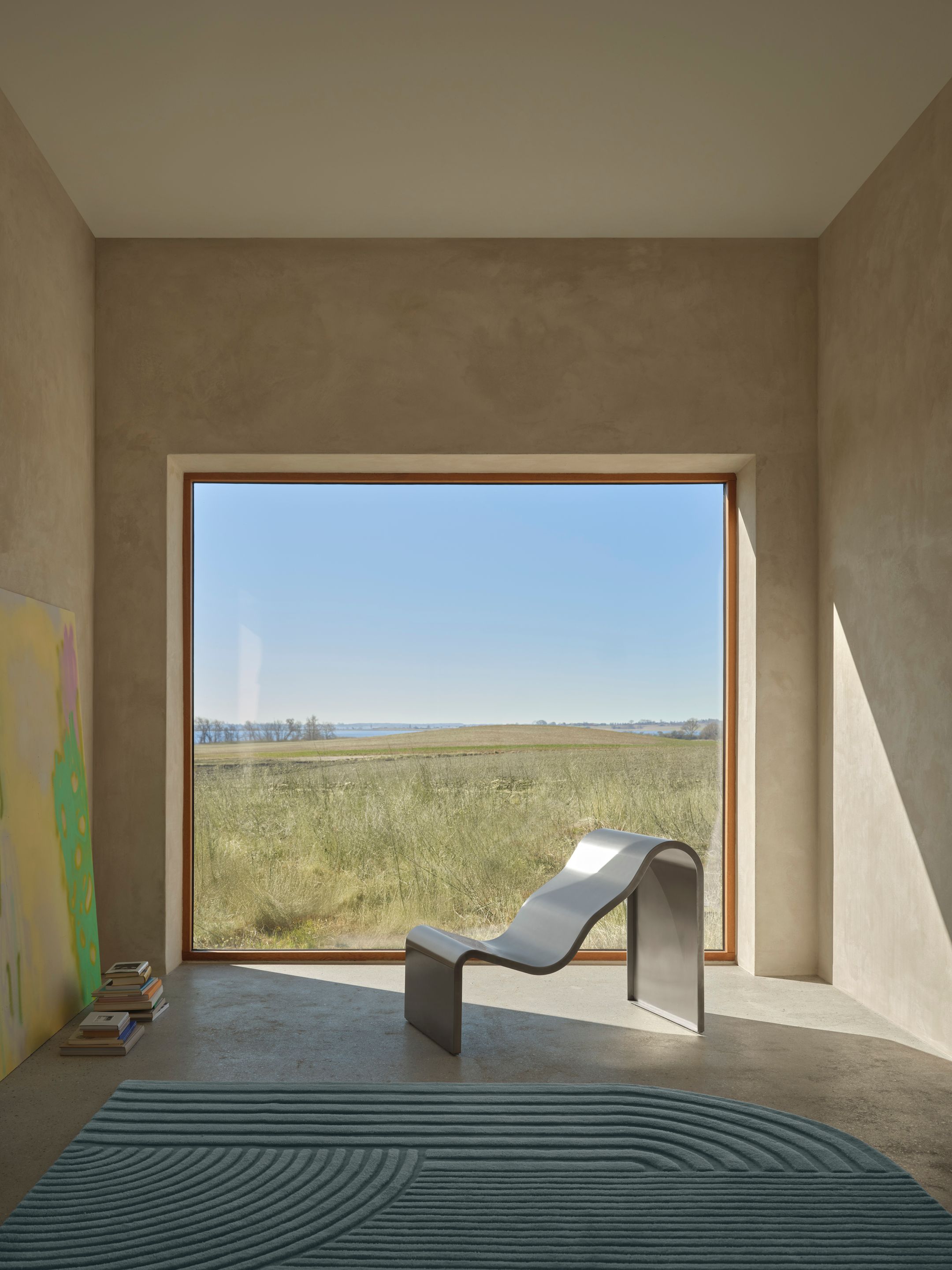 Dream View Bench de Lise Vester pour Muuto installée devant une grande fenêtre panoramique, assise sculpturale en acier inoxydable conçue pour la contemplation et le ralentissement.